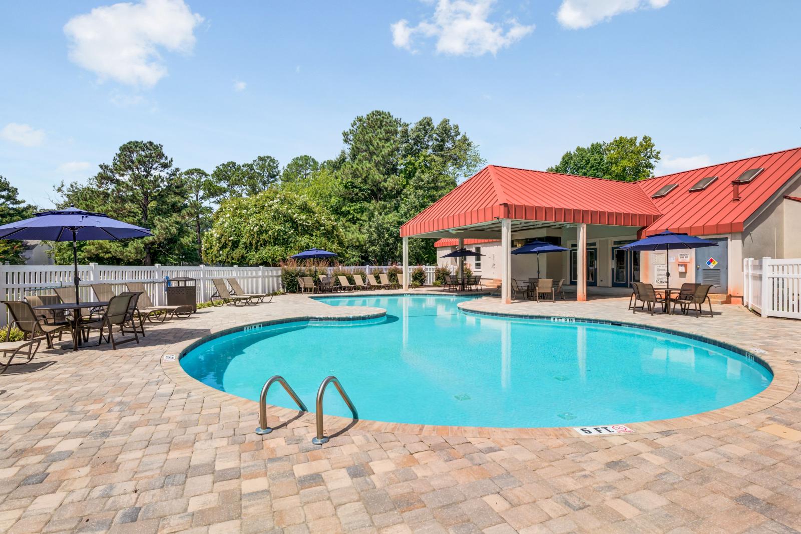 Outdoor swimming pool at The Samuel with lounge chairs, shaded tables, and a red-roofed pavilion surrounded by lush greenery