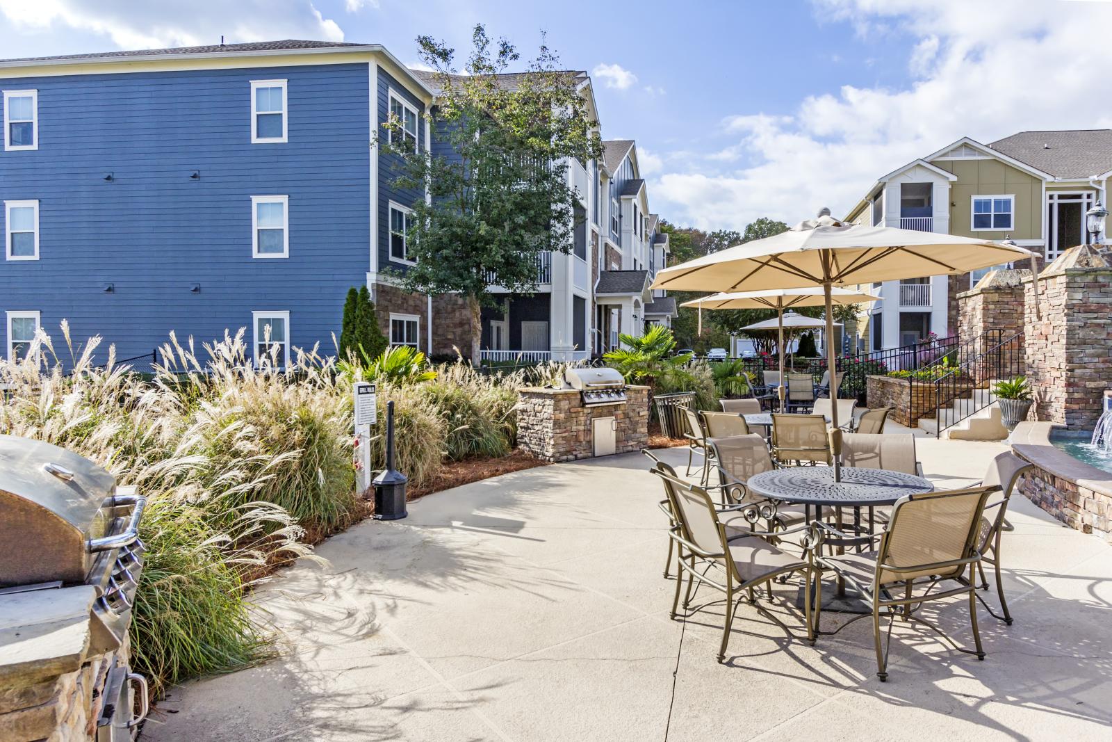 Grill and patio area with umbrella-shaded tables and lush landscaping