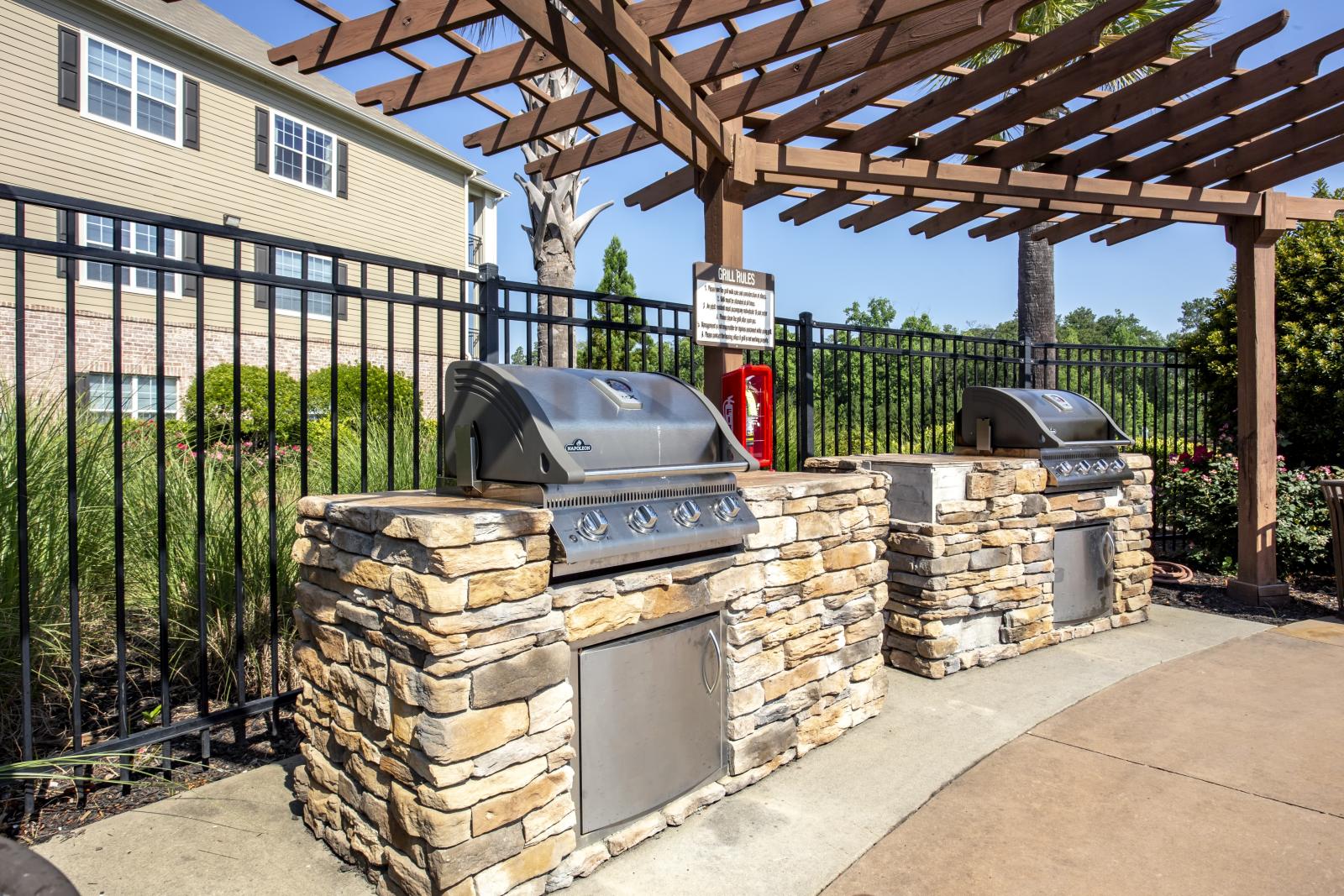 Close-up of outdoor grilling station with stone base and stainless steel appliances beneath a wooden pergola at Lauren Ridge community area.