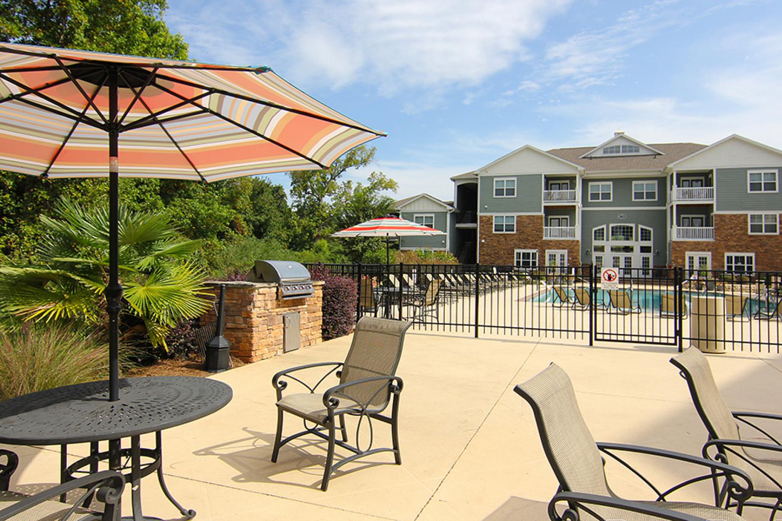 Shaded outdoor grilling and dining area with umbrellas and patio furniture at Reed Creek Apartments.