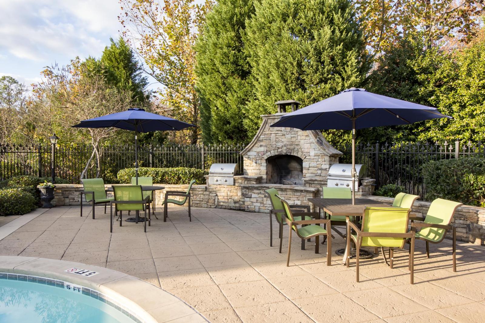 Poolside grilling station and dining area at The Heights at Lake Murray featuring stone fireplace, stainless steel grills, and umbrella-covered seating