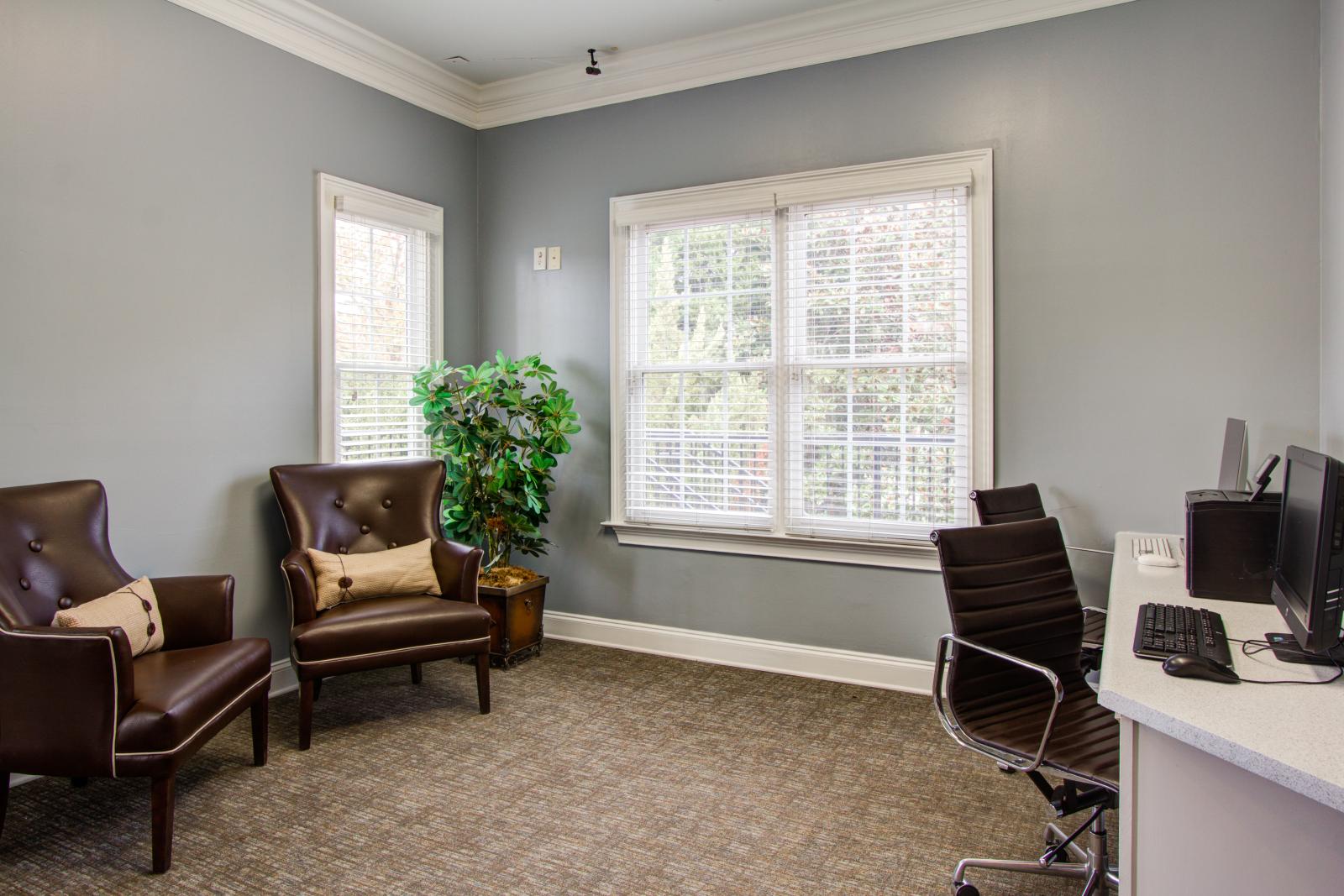 Resident business center at The Heights at Lake Murray featuring leather lounge chairs, computer workstations, and large windows with natural light.