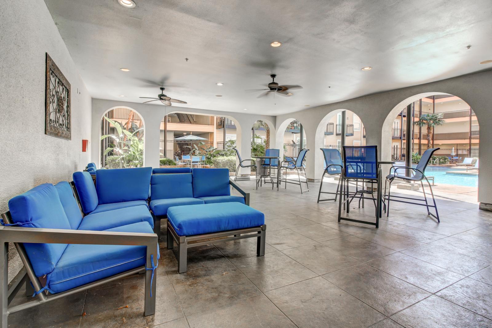 Covered outdoor lounge at The Saulet luxury apartments in New Orleans with modern blue cushioned seating and poolside views.