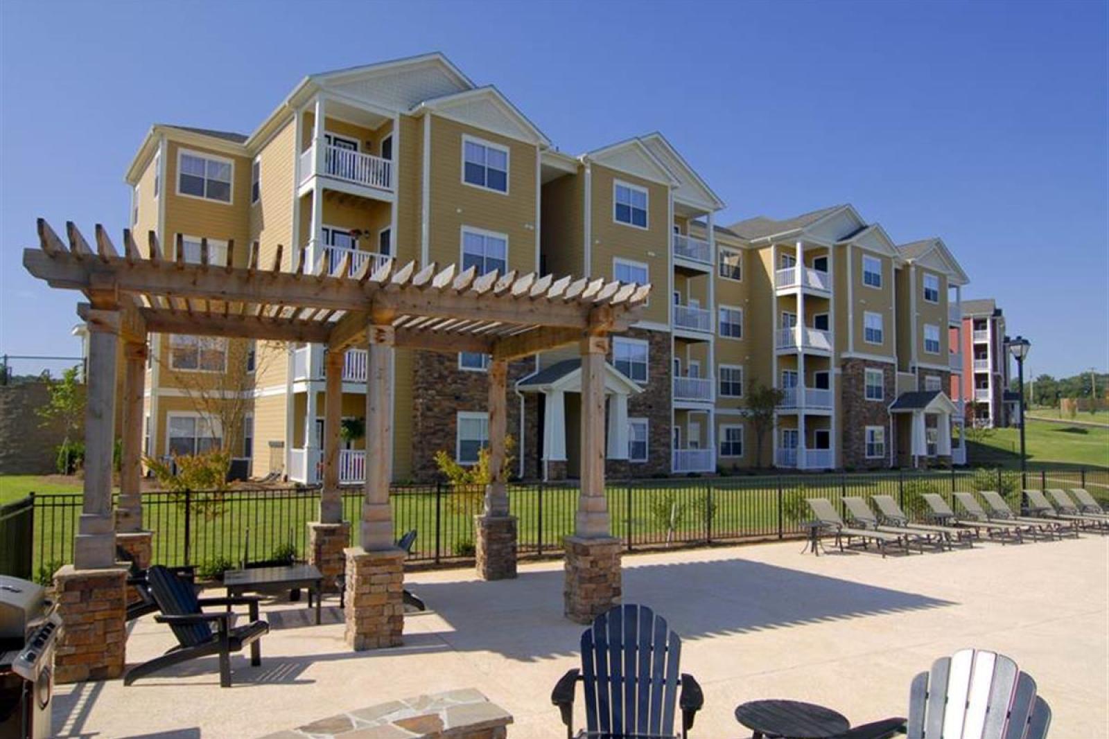 Modern four-story apartment buildings at Knob Creek Apartments with balconies, stone accents, and a pergola-covered seating area.