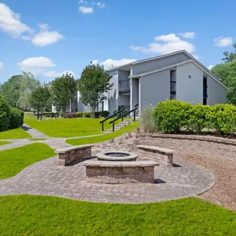 A building with a fountain in front, surrounded by grass and landscaping, with trees and a clear sky above.