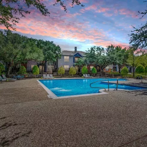 Stunning community pool captured at sunset, with vibrant skies reflecting on the water. The well-lit space offers a serene evening ambiance for relaxation or a refreshing swim.