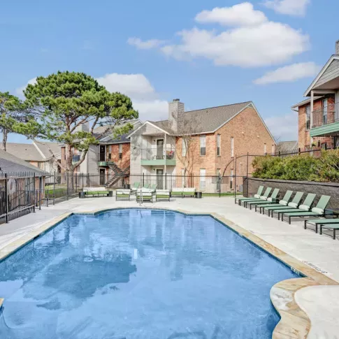  Refreshing outdoor pool with lounge chairs surrounding the clear blue water, set against a backdrop of modern apartment buildings and green trees. The bright blue sky enhances the relaxing atmosphere of the pool area.
