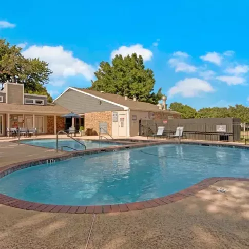 A swimming pool with a clubhouse in the background and lounge chairs arranged along the pool deck.
