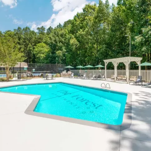 A refreshing outdoor pool with "The Forest Apartments" branding, surrounded by lush greenery and lounge chairs.