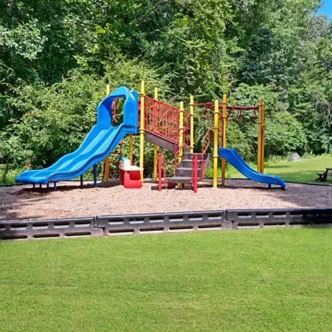 A children's playground with colorful slides and swings surrounded by greenery.