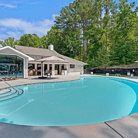 An outdoor swimming pool with forested surroundings and a clubhouse in the background.