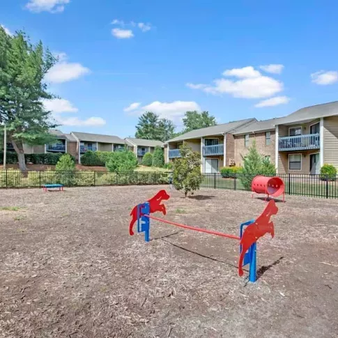 A small pet park featuring red horse-shaped seesaws and a fenced-in area with nearby apartments.