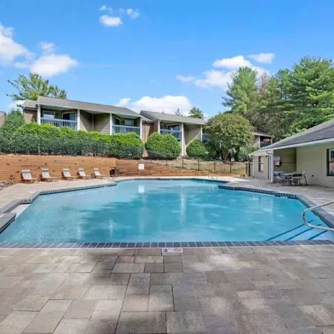 A crystal-clear swimming pool with paved surroundings and cozy seating, nestled among residential units.