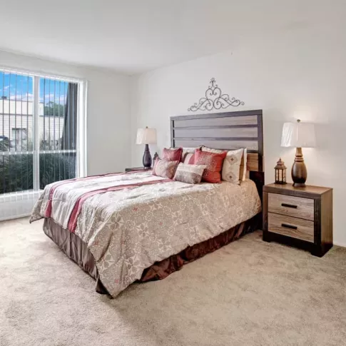 A serene bedroom with a large window, a patterned bedspread, and minimalist furniture.