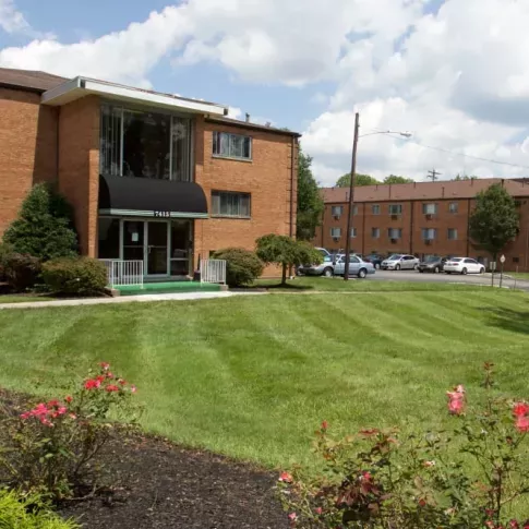 An exterior view of a brick apartment complex with well-maintained green lawns and colorful flowerbeds.