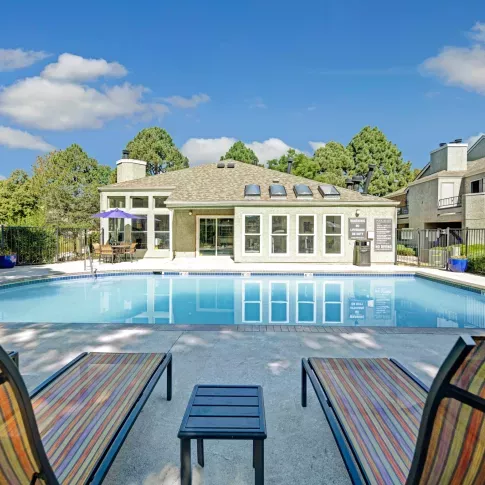 Relaxing pool area with colorful lounge chairs and umbrellas, offering a peaceful setting with a clear blue pool and a well-maintained clubhouse in the background at Waterfield Court Apartment Homes.