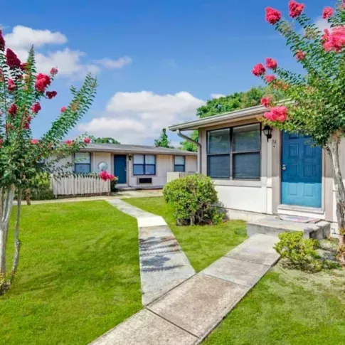 A landscaped pathway leading to single-story apartments with colorful crepe myrtle trees in full bloom and vibrant green grass surrounding the area.