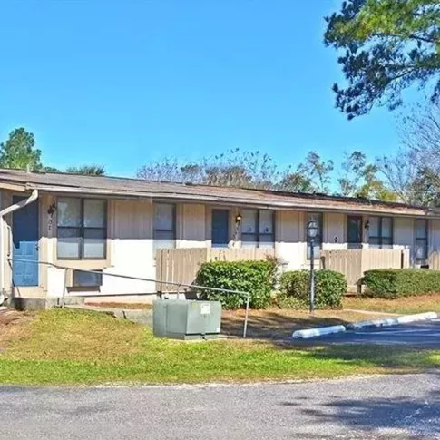 A well-maintained row of single-story apartment units with fenced patios, landscaped greenery, and a nearby parking area under a clear blue sky. This image highlights the practical and serene living environment at Broadview Oaks Apartments.