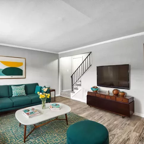 Fully staged living area at Maple Bay Apartments, featuring modern furniture, a mounted TV, and access to the dining area.