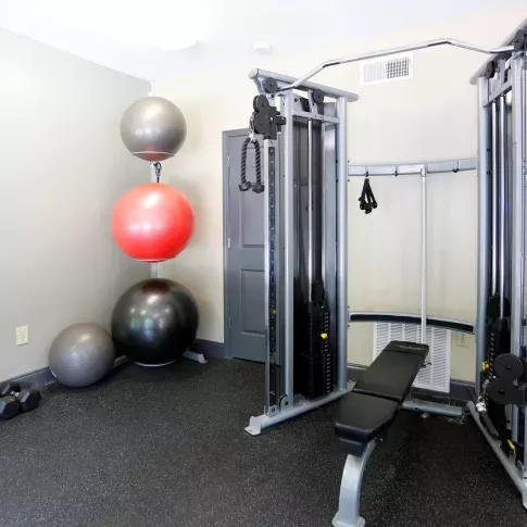 A fully equipped fitness center at Norcross Crossings Apartments featuring modern exercise machines, free weights, and yoga balls, with large windows providing natural light.