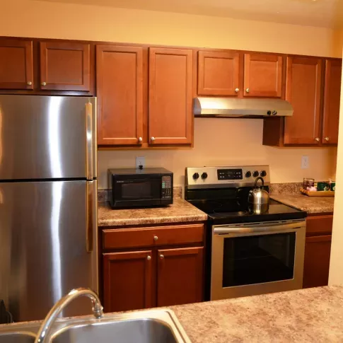 A modern kitchen at North River Place Apartments featuring stainless steel appliances, wooden cabinetry, and a polished countertop