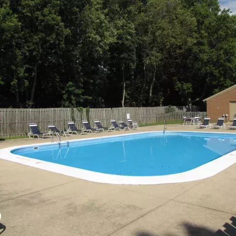 The outdoor pool area at North River Place Apartments, surrounded by lounge chairs, fencing, and trees, offers a refreshing retreat for residents