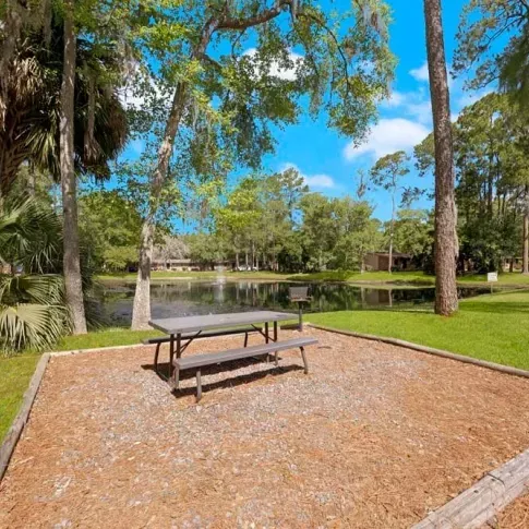 A serene picnic area surrounded by trees, overlooking a pond.