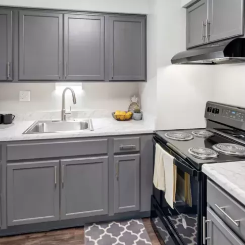 Another angle of a modern kitchen featuring gray cabinetry, a stove, and a tiled backsplash.