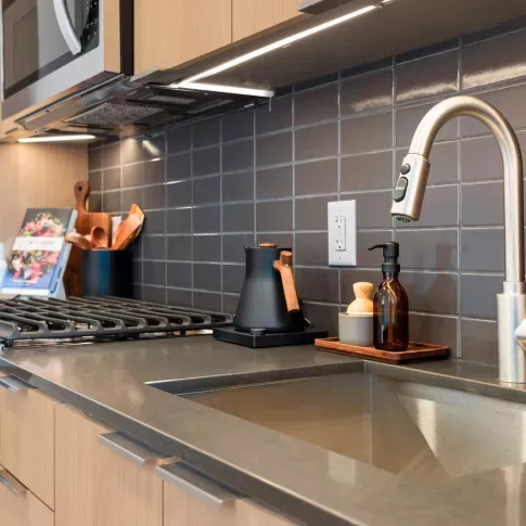 Modern kitchen featuring stainless steel appliances, wood cabinetry, and a sleek tile backsplash at The Edmund Apartments.