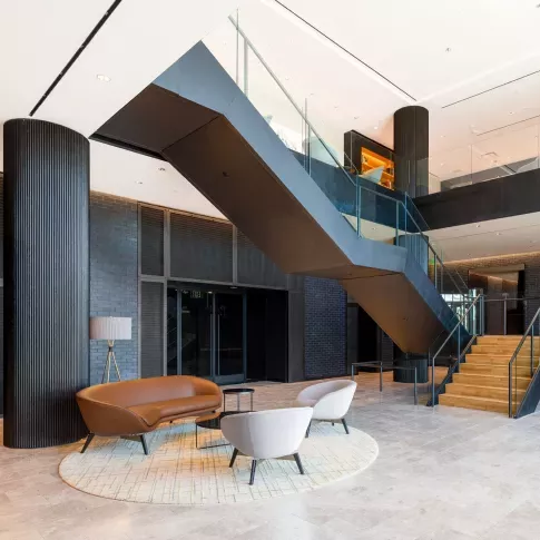 An elegant meeting space featuring a combination of blue and brown contemporary chairs, accent lighting, and a warm wooden floor.
