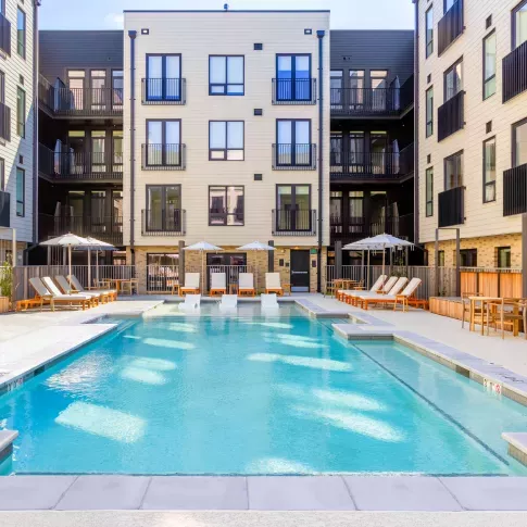 Outdoor pool area at The Edmund Apartments featuring lounge chairs, umbrellas, and in-pool seating surrounded by modern apartment buildings.