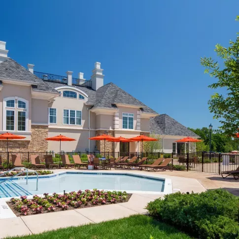A vibrant outdoor pool area at The Grove Somerset Apartments, featuring cozy lounge chairs, bright orange umbrellas, and a beautifully landscaped backdrop.