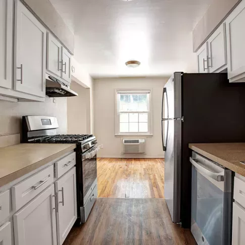 Modern galley kitchen with white cabinetry, stainless steel appliances, and natural light flowing in through a window, showcasing a cozy and functional layout.