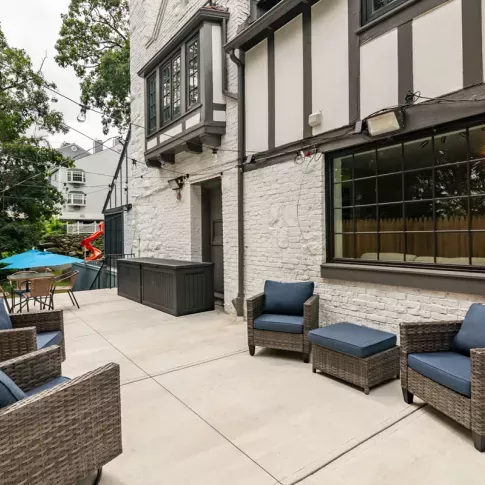 An outdoor patio area featuring cozy wicker chairs with blue cushions, a table with an umbrella, and a charming Tudor-style building in the background.