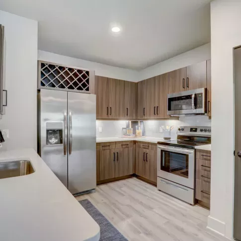 A fully equipped kitchen with sleek cabinetry, a wine rack, and stainless steel appliances in a Tropia Wellen Park apartment.