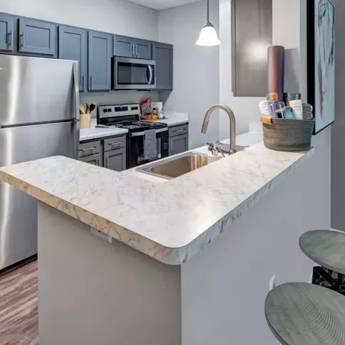 Modern kitchen at Trotter's Landing Apartments with stainless steel appliances, marble-patterned countertops, and sleek gray cabinetry.