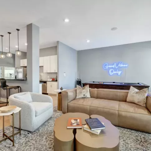 Stylish clubhouse with cozy seating, a billiards table, and a neon sign reading "Good Vibes Only."