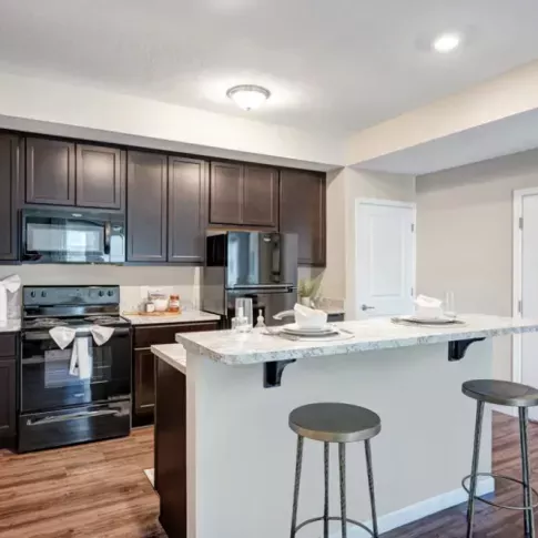 A stylish open-concept kitchen with a breakfast bar, barstools, and dark wood cabinetry in a Walden Lakes apartment.
