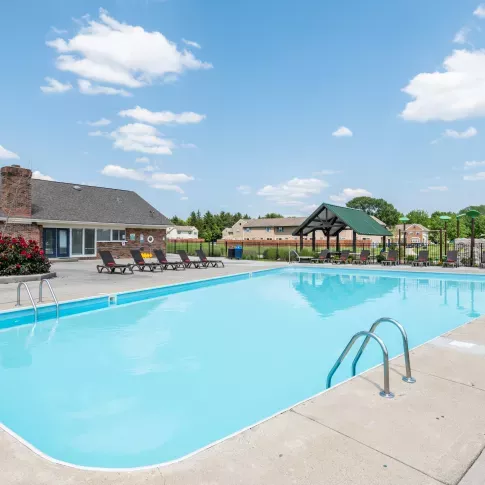 Outdoor swimming pool at Worthington Meadows Apartments with surrounding lounge chairs, a covered pavilion, and a landscaped community backdrop.