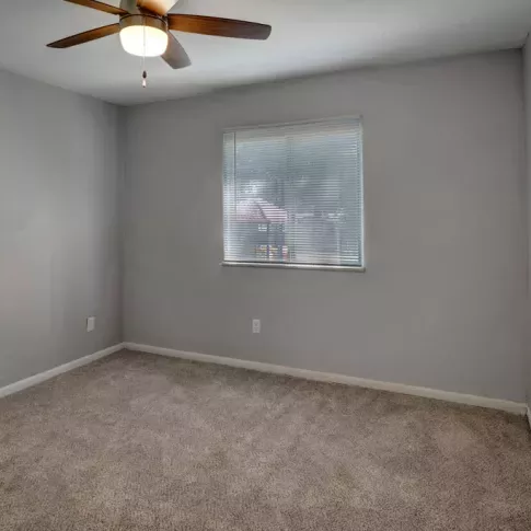 A secondary bedroom at Yearling Plaza Apartments in Columbus, OH, featuring neutral tones, a ceiling fan, and natural lighting from the windows.