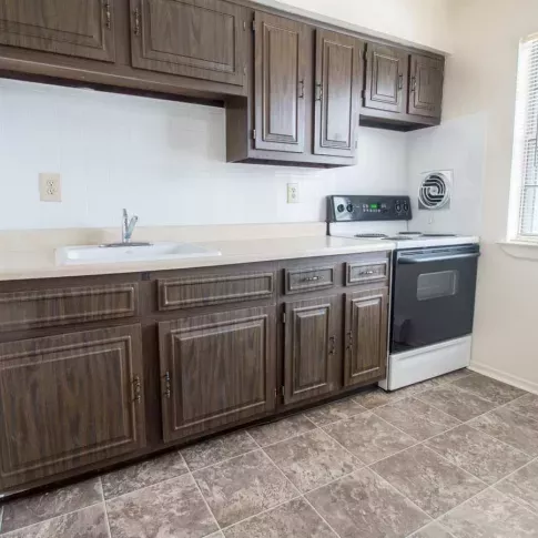 Kitchen area at Washington Gardens Apartments in Washington, NJ, featuring dark wood cabinetry, a single sink, a stove, and a large window allowing natural light.