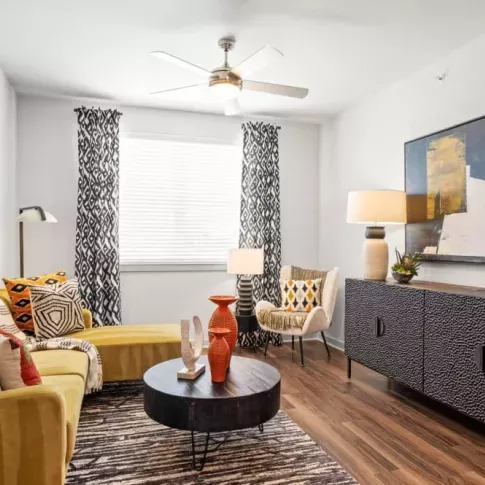 A modern living room featuring a yellow sectional sofa, patterned curtains, and abstract artwork on the walls.