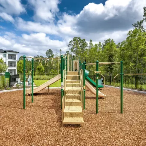 A well-maintained playground with slides and climbing structures, surrounded by nature.
