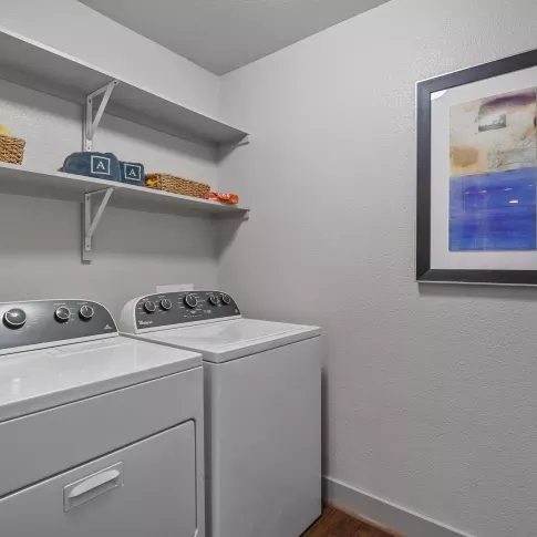 Spacious in-unit laundry room featuring modern Whirlpool washer and dryer with additional shelving for storage and organization.