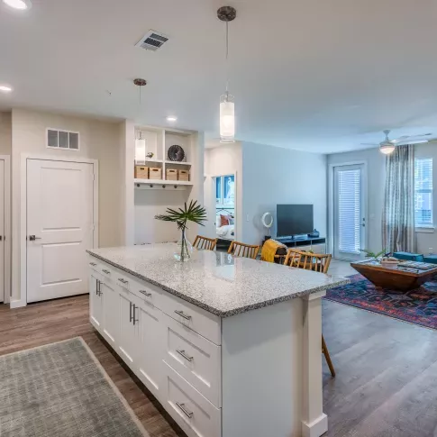 A modern kitchen featuring white cabinetry, stainless steel appliances, granite countertops, and pendant lighting over a spacious island with wooden barstools.