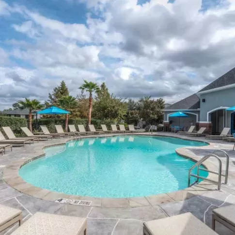 Sparkling blue pool with a stone-accented deck at The Landings of Conroe, featuring comfortable lounge chairs and shaded seating areas for relaxation.
