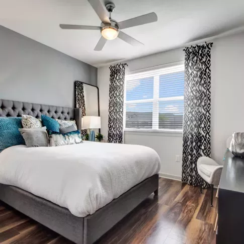 Elegant bedroom with a tufted gray headboard, cozy bedding, and a large window allowing natural light to brighten the space.