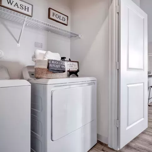 A well-organized laundry room with a washer and dryer, floating shelves, and charming decorative signs for a functional and stylish space.