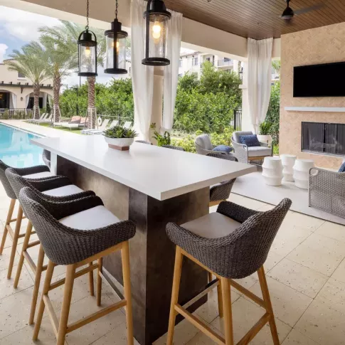 A modern outdoor bar with high-top seating and a cozy fireplace seating area, creating the ultimate entertainment space by the pool.
