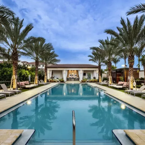 A luxurious swimming pool lined with palm trees and sun loungers, leading to a stylish poolside lounge with cabana seating at Locklyn West Palm Luxury Apartments.